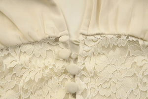 Close-up detail of beige lace splicing chiffon fabric with delicate fabric-covered buttons