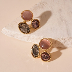 Gros plan de boucles d'oreilles géométriques œil de chat gris et rose sur pierre blanche