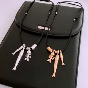 Minimalist silver and gold fish bone pendant necklaces on black leather texture