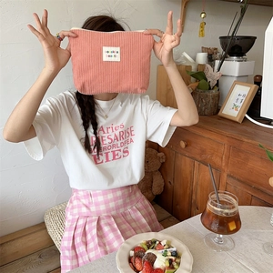 Pink corduroy makeup bag with embroidered label next to a white t-shirt and plaid skirt