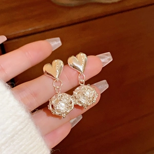 Detail showing gold heart earrings with hollow round pendants held in hand for close-up