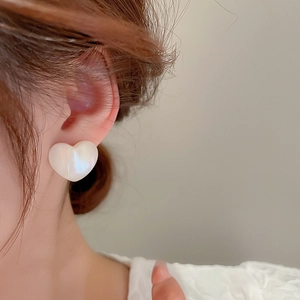 Macro shot of a heart-shaped earring with iridescent pearl luster on model's ear