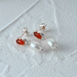 Macro shot of s925 silver earring featuring a red gemstone and a dangling pearl drop