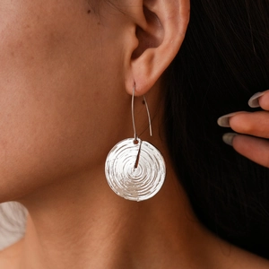Detail view of silver geometric disc earrings with concentric textures worn by a model