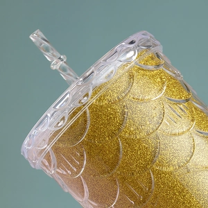 Detailed macro view of golden glitter layer and mermaid scale texture on plastic straw cup