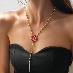 Detail of a gold bead Y-necklace featuring a red flower pendant on a female model