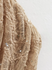 Gros plan sur un tissu en dentelle beige avec découpes et accents de strass scintillants
