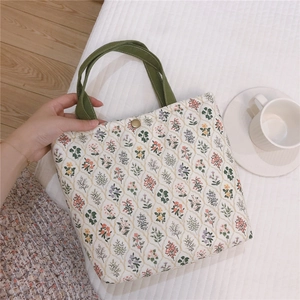 Vue de dessus d'un sac à lunch matelassé à fleurs avec anses vertes et bouton doré