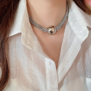 Close-up of a layered silver metal chain necklace with a large ball pendant on model