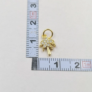 Macro shot of gold palm tree pendant with clear zircons next to scale measurement