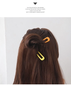 Detail showing bright orange and yellow U-shaped hairpins on dark brown hair