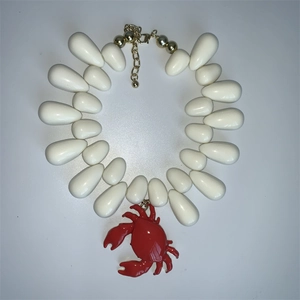 White teardrop beaded necklace featuring a red crab pendant with a golden metal clasp