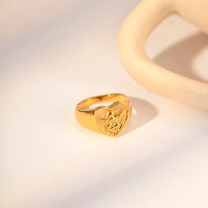 Close-up of heart-shaped gold ring featuring an intricate angel relief on a warm backdrop