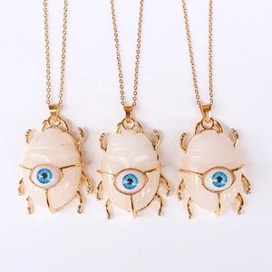 Macro detail of three beetle pendants in white stone and gold frame with blue eyes