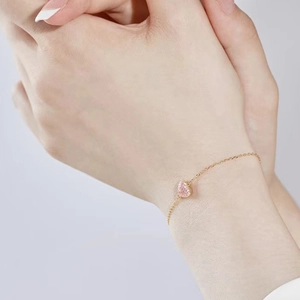 Detail of a golden chain bracelet featuring a pink heart-shaped zircon pendant on wrist