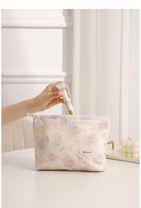 Close-up of floral canvas makeup bag with top zipper and brand label on white desk