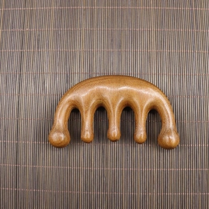 Close-up of five-tooth sandalwood scalp massager with natural wood grain on bamboo mat