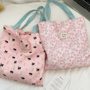 Close-up of pink floral and cat embossed tote bags with blue handles and textile labels