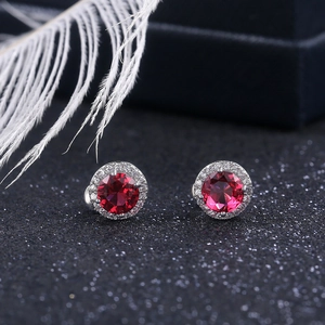 Detail of round red zircon stud earrings with halo setting on a black textured background