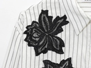 Close-up of intricate black floral lace applique on a white striped cotton blouse