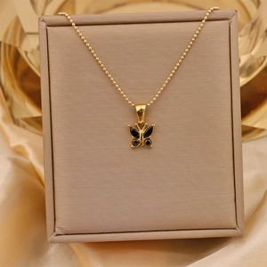 Detail of 18K gold-plated butterfly pendant with black zircon stones on a beige stand