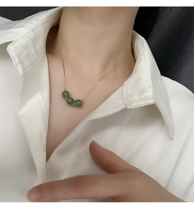 Close-up of three green jade beads on a minimalist gold chain worn on a neck