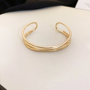 Macro detail of minimalist multi-layer overlapping gold wave bangle with a sleek C-shaped open design