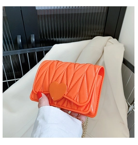 Detail of bright orange heart-shaped quilted silicone mini bag with golden chain strap