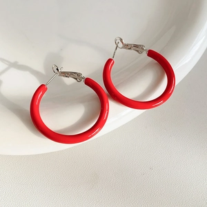 Detail of red enamel hoop earrings resting on white ceramic tray with polished finish