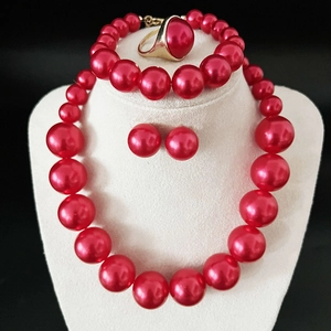 Detailed set of red faux pearl necklace, bracelet, earrings and golden ring on bust display