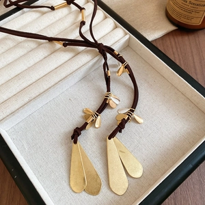 Macro detail of golden teardrop pendants on brown suede cord necklace set