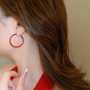 Close-up of vibrant red oversized hoop earrings worn by a model in warm lighting