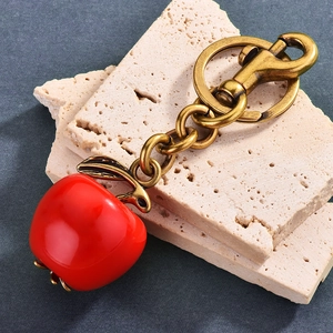 Polished red apple keychain with bronze metal horseshoe buckle on beige travertine stone