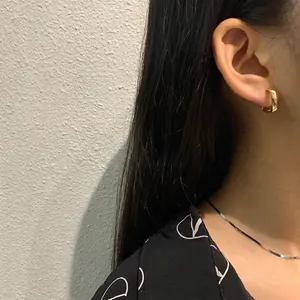 Close-up of model wearing gold twisted hoop earrings and a sleek flat chain necklace