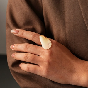 Gros plan d'une grande bague en résine irrégulière avec bordure dorée sur le doigt d'un modèle
