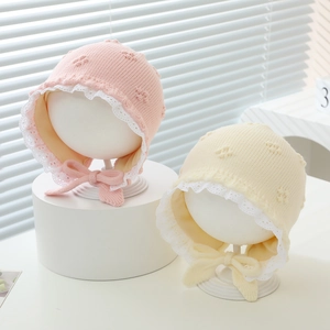 Close-up of knit baby hats with lace trim and bow straps in pink and beige colors