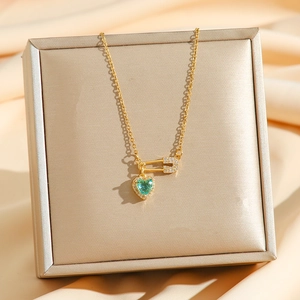 Detailed view of a gold safety pin necklace with a sparkling green heart pendant