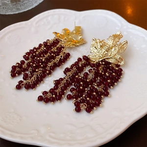 Detail of vintage gold leaf earrings with red grape-shaped bead tassels on a white plate
