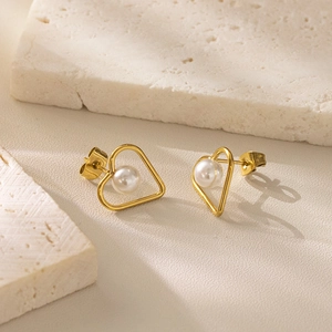 Elegant gold heart-shaped stud earrings with centered pearl on aesthetic stone background