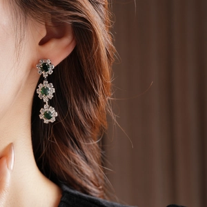 Close-up of triple-layered silver earrings with green gemstones and diamond accents