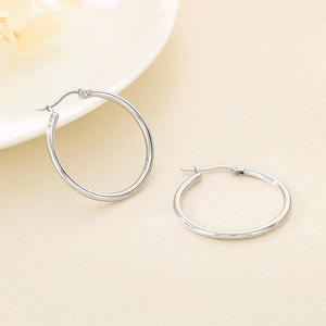 Detailed close-up of polished silver hoop earrings on a minimalist textured background