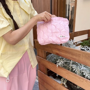 Close-up of pink quilted cosmetic bag with sozakka label in a natural garden setting