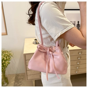 Pink drawstring bucket bag with bow detail shown on a model in a warm home setting