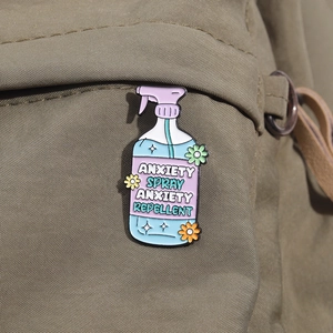 Close-up of anxiety spray enamel pin attached to a canvas backpack strap