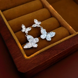 Detailed close-up of butterfly crystal earrings in a velvet-lined wooden jewelry box