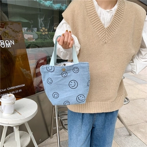 Outdoor shot of a light blue corduroy handbag with smiley patterns and magnetic closure