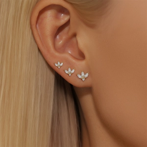 Close-up of three gold leaf-shaped studs with clear stones worn on a model's ear