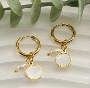 Detail of gold hoop earrings with white shell and baroque pearl charms on white background