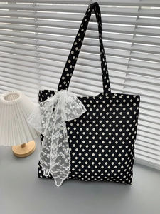 Detail of black polka dot canvas tote bag featuring a white lace bow and shoulder strap