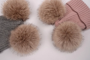 Détail de deux pompons en fausse fourrure sur des bonnets tricotés gris et roses